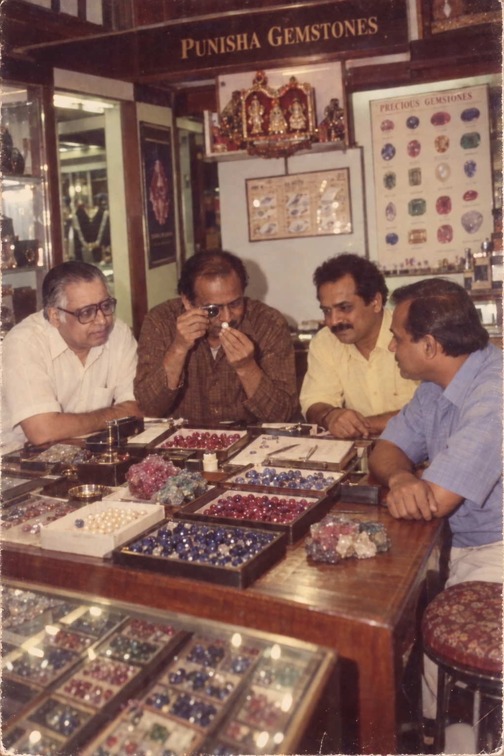 A gemstone examination at the Punisha Gemstones counter, surrounded by trays of coloured stones.